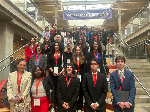 A goupr of students in business attire stand at the bottom of the stairs